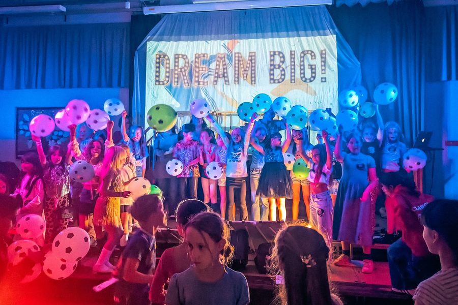 Children on stage holding football balloons in front of a Dream Big! backdrop