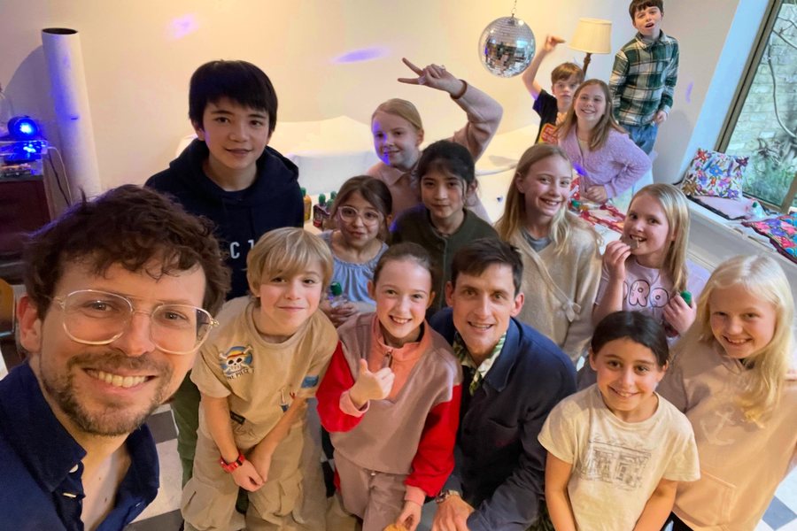 Dom James and Tommy Antonio taking a selfie with a big group of smiling children from the chorus